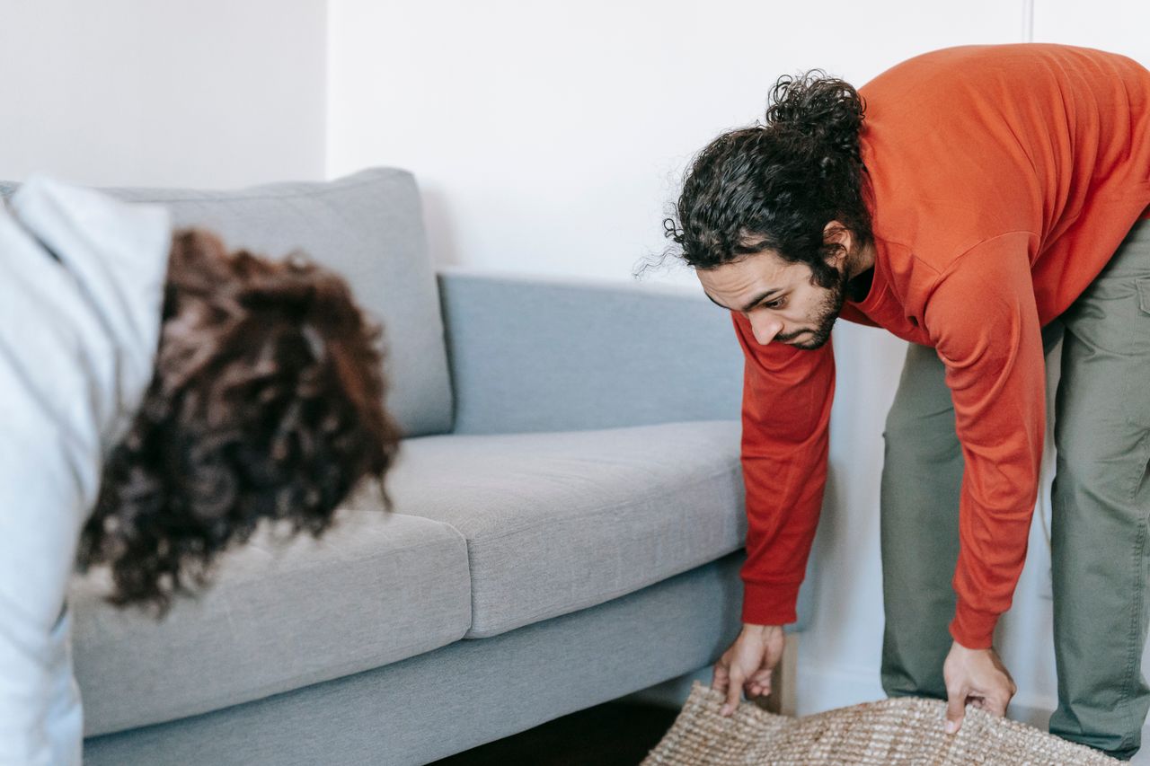 Un couple range son salon, en réorganisant meubles et tapis ensemble, avec esprit d’équipe.